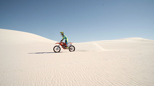 Young motocross racer doing a wheelie on sand dunes