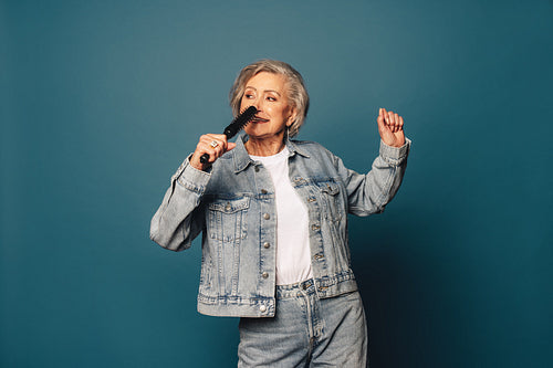 Cheerful mature woman enjoying a playful dance routine on a blue background