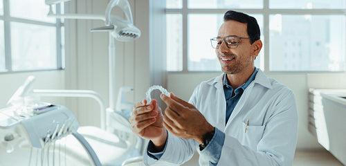 Male dentist examining clear aligner in modern dental clinic portrait