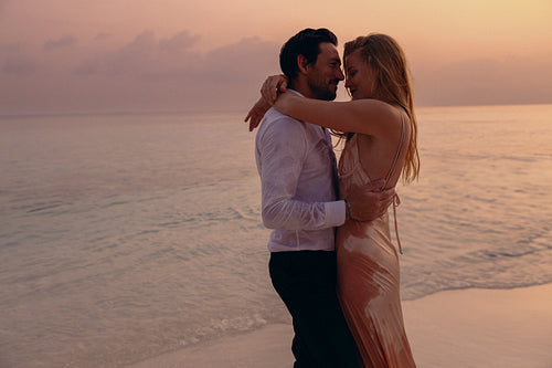 Young couple embracing on a honeymoon at a beach during sunset