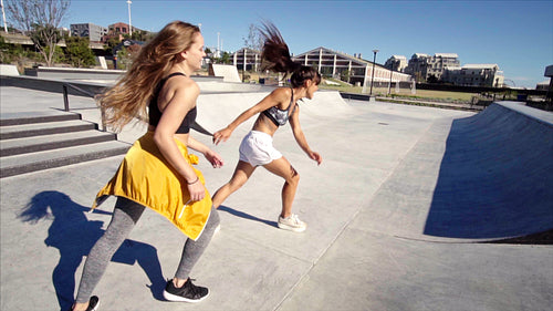 Two active young women running around a skate park