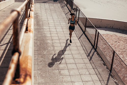 Female athlete running on seaside boardwalk
