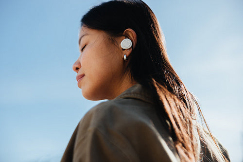 Woman listening with earbuds outdoors, peaceful sky backdrop