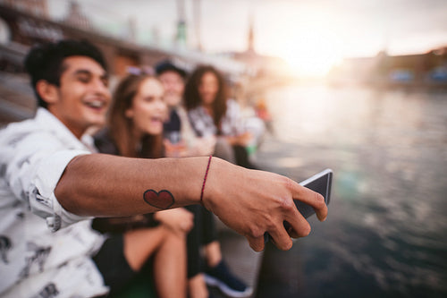 Young man with friends taking selfie by the lake