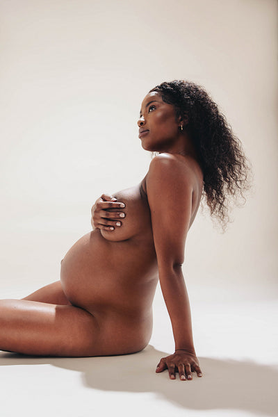 Confident dark-skinned pregnant woman showing off her nude maternity body in a nude studio
