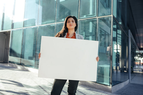 Confident businesswoman holding a white banner outside her workplace
