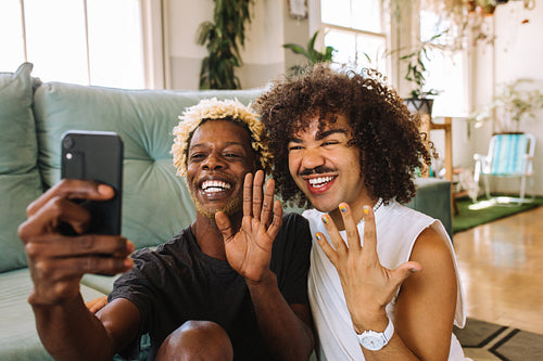 Cute young gay couple video calling their friends at home