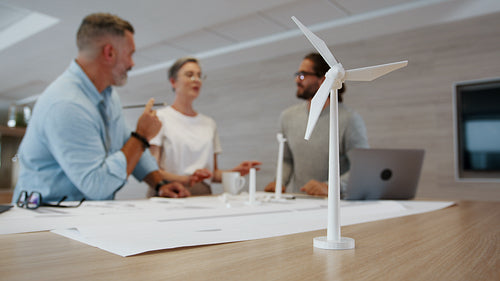 Experts in sustainable engineering work together as a team, reviewing blueprint drawings for a windmill design