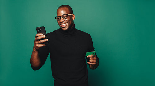 Happy young man using a green credit card for online shopping on his mobile phone