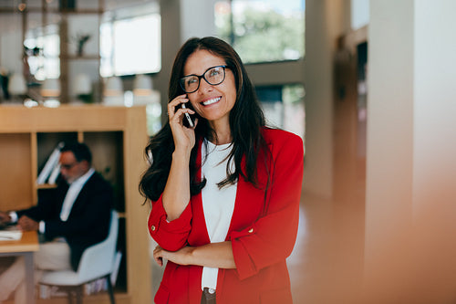 Confident woman in red blazer on phone in professional office setting