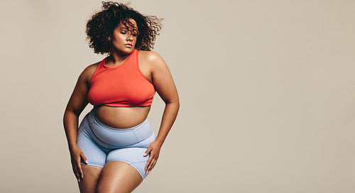 Self-assured woman standing in a studio, wearing sports clothing and embracing her fit body