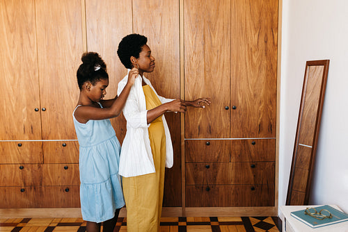 Girl helping her mom get dressed in front of the mirror at home