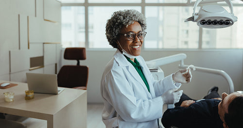 Smiling dentist holding dental aligner during senior patient consultation