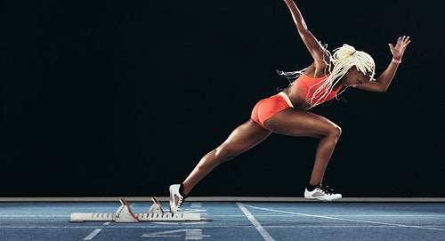Female sprinter taking off from starting block on a running track