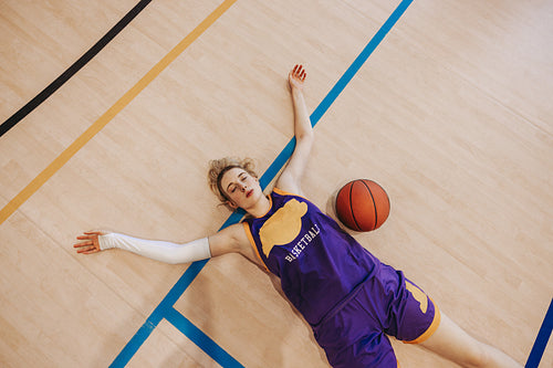 Exhausted female basketball player lying on court floor with basketball
