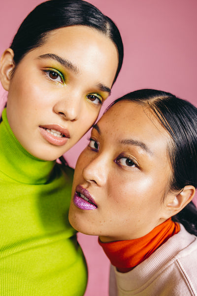 Two women wearing striking makeup taking a selfie together in a studio