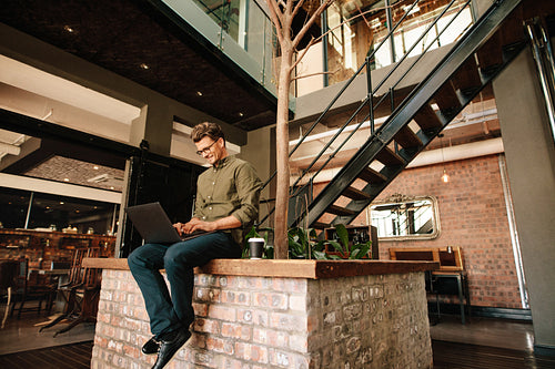 Young man sitting in office cafeteria working on laptop