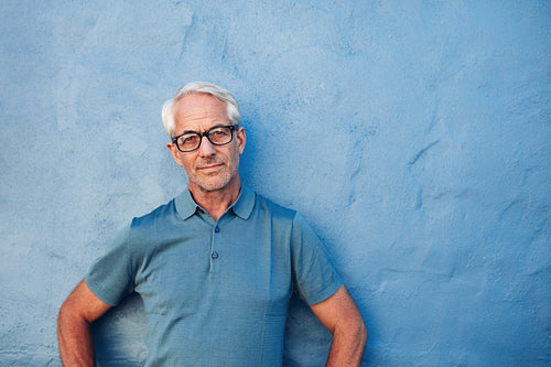 Mature man standing against a blue wall