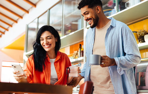 Smiling Latin American couple enjoying coffee and a smartphone together at home
