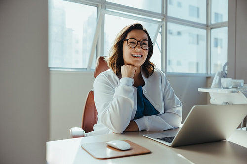 Female dentist manages clinic tasks using laptop at her desk