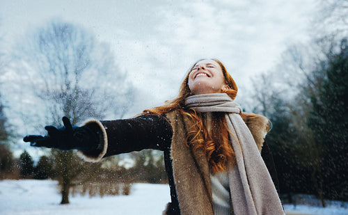 Redhead woman reaches for snow in a winter coat outdoors