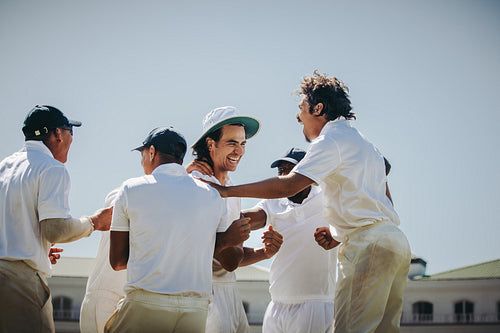 Team celebrating a young male player in a cricket match outdoors
