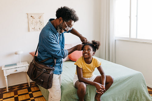 Father styling his daughter's Afro hair a in bedroom