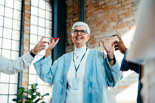 Mature woman smiling while playing with co-workers in a modern office environment