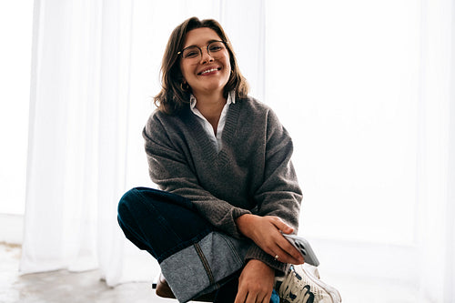 In a bright workspace, the woman uses a smartphone while sitting on the floor