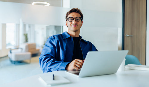 Man at laptop in blue jacket at office