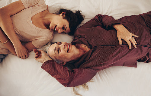 Top view of smiling mother and daughter lying on bed facing each other