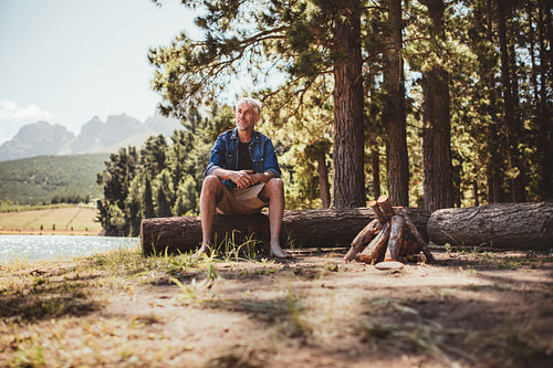 Mature man sitting on a log staring out to the lake