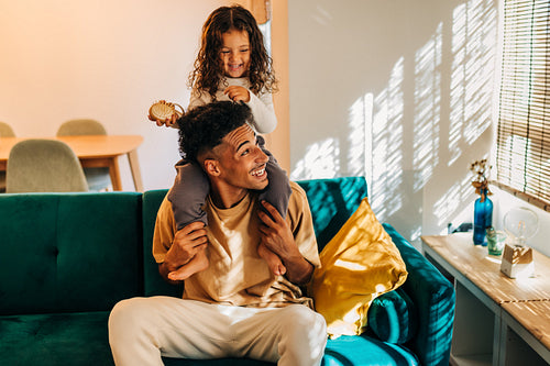 Playful young father carrying his daughter on his shoulders at home
