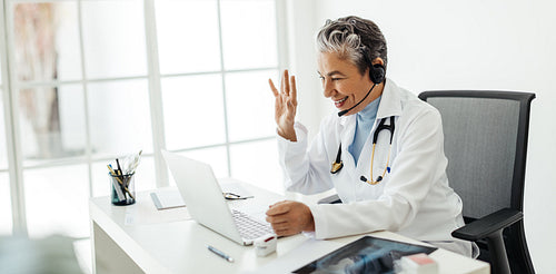Virtual doctor’s appointment: Friendly female health professional waving to a patient over a video call