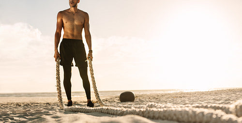 Man standing on the beach holding battling ropes for workout