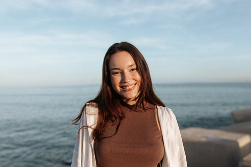 Pretty brunette woman smiling at the camera by the seaside