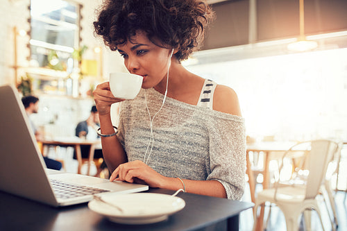 Young african woman drinking coffee and using laptop at a cafe