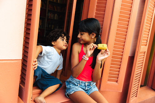 Sibling bonding moments featuring kids enjoying food by vibrant Latin American windows
