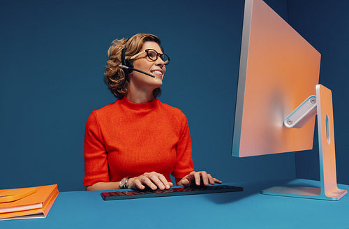 Mature woman in eyeglasses and headset working at desk while communicating