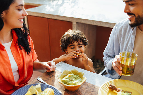 Family enjoying a meal outdoors with a happy child eating