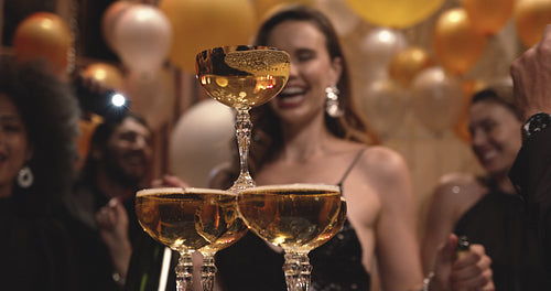 People dancing around pyramid of champagne glasses at party