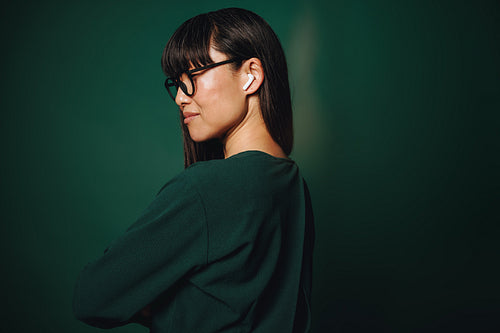 Confident woman with earbuds and glasses in studio portrait