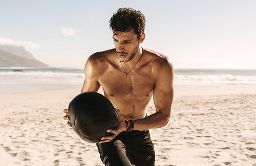 Man training at the beach using a medicine ball