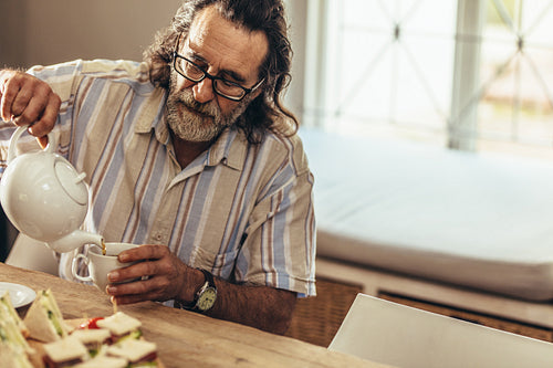 Elderly man with beard pouring tea in cup
