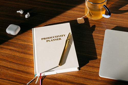 Productivity planner on desk with pen, tea and laptop in organized workspace