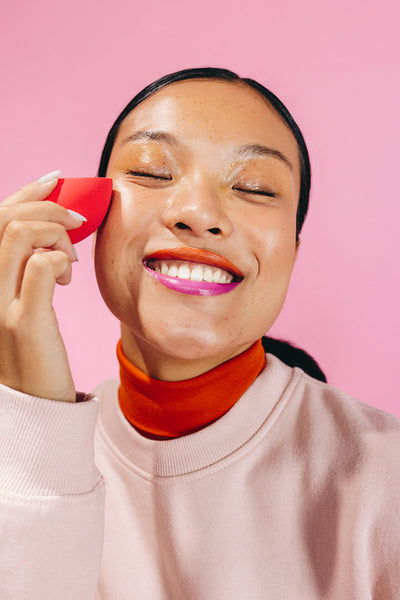 Joy with a beauty sponge, woman smiles as she blends makeup on her face