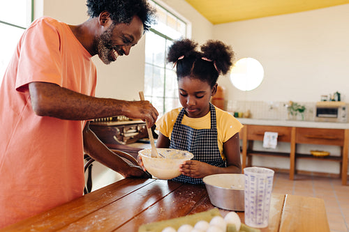 Father and daughter making a cake together at home