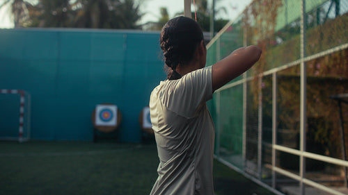 Young woman practicing archery, aiming an arrow with focus and determination at the target