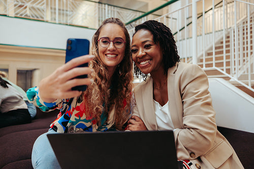Two joyful businesswomen taking a selfie together in a contemporary corporate setting