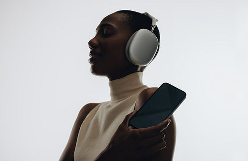 Silhouette of woman with headphones holding smartphone for mockups and music streaming